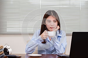 Beautiful asian woman drinking coffee in the morning before work and working on laptop computer
