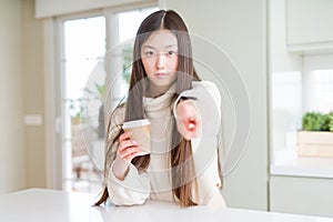 Beautiful Asian woman drinking a coffee in a take away paper cup pointing with finger to the camera and to you, hand sign,