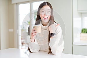 Beautiful Asian woman drinking a coffee in a take away paper cup pointing and showing with thumb up to the side with happy face