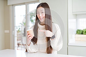 Beautiful Asian woman drinking a coffee in a take away paper cup very happy pointing with hand and finger