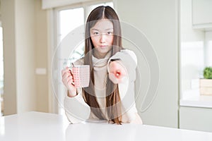 Beautiful Asian woman drinking a cup of coffee pointing with finger to the camera and to you, hand sign, positive and confident