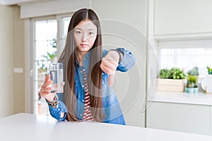 Beautiful Asian woman drinking a glass of fresh water with angry face, negative sign showing dislike with thumbs down, rejection