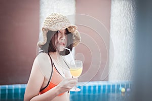 Beautiful Asian woman drinking orange juice at swimming pool,Happy and smiling,Relax time,Summer travel concept