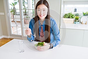 Beautiful Asian woman eating green fresh broccoli with a happy face standing and smiling with a confident smile showing teeth