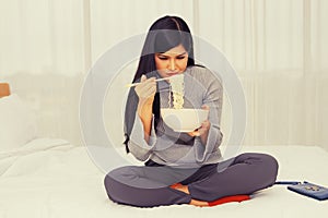 Beautiful Asian woman eats unappetizing food in bed because she has no money for good food.