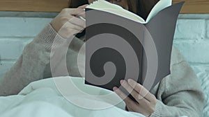 Beautiful asian woman enjoying drinking warm coffee and reading book on bed in her bedroom.