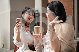 A beautiful Asian woman enjoys talking and having coffee with her friend while sitting on the stairs