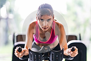 Beautiful Asian woman exercising on stationary cycling machine in indoor fitness gym, determination face. Sport training concept