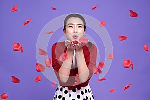 Beautiful Asian woman with expressing happiness in valentine`s day. girl blowing rose petals from her hands on purple background