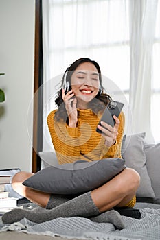 Beautiful Asian woman eyes closed, smiling, listening to music through headphones