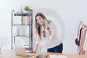 Beautiful asian woman fashion designer standing in the clothing store and studio. In front of the laptop and using smartphone.