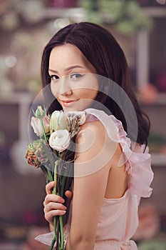 Beautiful asian woman florist in pink dress with bouquet of flowers in hands in flower store