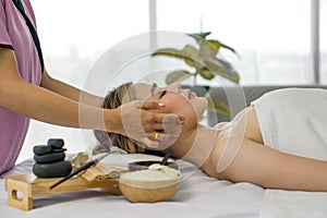 Beautiful asian woman getting face massage in beauty spa. Young woman with closed eyes relaxing in indoor spa while getting head