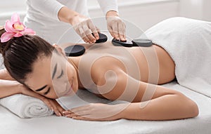 Beautiful asian woman getting massage with hot stones at modern spa salon