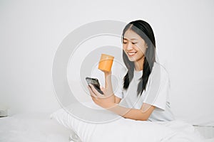 Beautiful Asian woman has woken up on a white bed and holding coffee in the morning at home in morning lifestyle concept