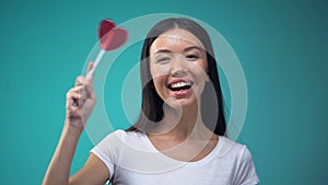 Beautiful asian woman having fun holding big heart-shaped lollipop, template