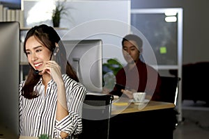 Beautiful Asian woman with headphones work night shift at call center customer care service desk, looking at desktop computer,