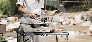 Beautiful Asian woman in her 30s preparing food Grill pork chop steak for dinner on the picnic grill. Adventure camping