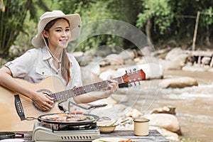 Beautiful Asian woman in her 30s preparing food Grill pork chop steak for dinner on the picnic grill. Adventure camping