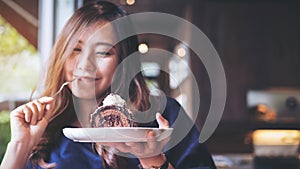 A beautiful Asian woman holding chocolate cake roll and whipped cream and fork with feeling happy and enjoy eating in the cafe