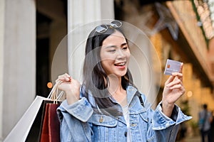 Beautiful Asian woman holding credit card and carrying shopping bags while shopping at city mall