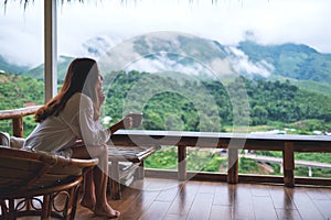 A beautiful asian woman holding and drinking hot coffee on balcony , looking at mountains and green nature