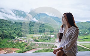 A beautiful asian woman holding and drinking hot coffee on balcony , looking at mountains and green nature