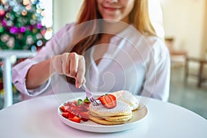 A beautiful asian woman holding and eating pancakes with strawberries and whipped cream