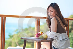 A beautiful asian woman holding fruits while enjoy sitting at balcony