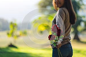 A beautiful asian woman holding and giving red roses flower in the park