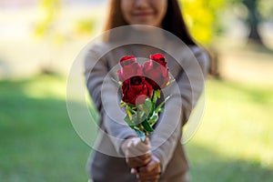 A beautiful asian woman holding and giving red roses flower in the park