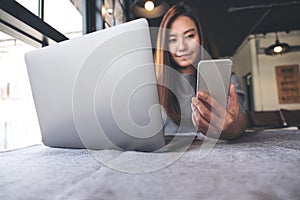 A beautiful Asian woman holding and looking at mobile phone while using laptop in cafe