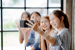 Beautiful Asian woman holding a mobile phone up to take pictures with a group of friends at work, taking pictures using a new