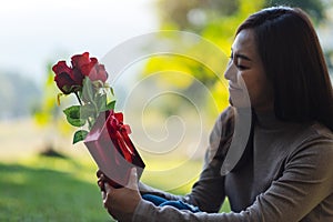 A beautiful asian woman holding red roses flower and a gift box in the park