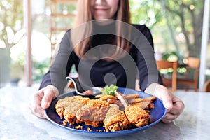 A beautiful asian woman holding and showing a plate of fried chicken and french fries in restaurant