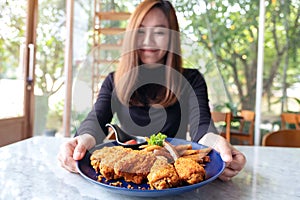 A beautiful asian woman holding and showing a plate of fried chicken and french fries in restaurant