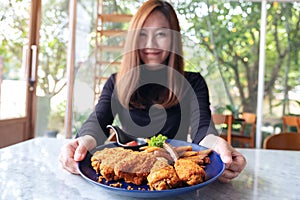 A beautiful asian woman holding and showing a plate of fried chicken and french fries in restaurant