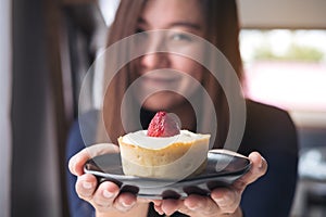 A beautiful Asian woman holding and showing strawberry cheese tart with feeling happy in the modern cafe