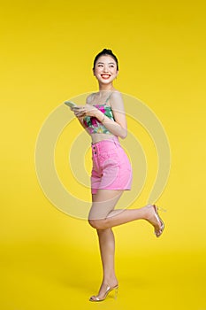 Beautiful Asian woman holding smartphone and smiling on light yellow background