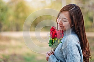 A beautiful asian woman holding and smelling red roses flower with feeling happy on Valentine`s day