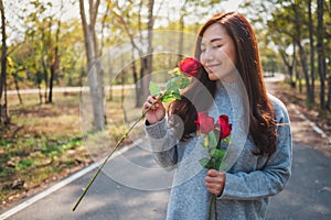 A beautiful asian woman holding and smelling red roses flower with feeling happy on Valentine`s day