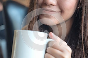 A beautiful Asian woman holding a white cup of hot coffee with feeling happy in cafe