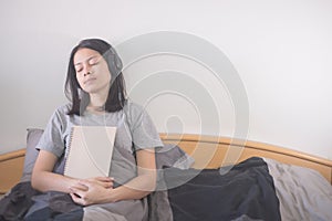 Beautiful Asian woman listening music with headphone and reading book relaxing on the bed.