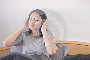 Beautiful Asian woman listening music with headphone relaxing on the bed..