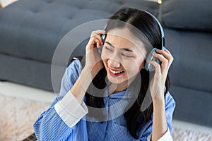 Beautiful asian woman listening to music on couch in living room at home. Happy asia female wearing headset and sitting on sofa