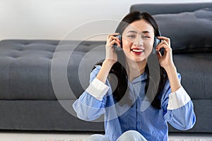 Beautiful asian woman listening to music on couch in living room at home. Happy asia female wearing headset and sitting on sofa
