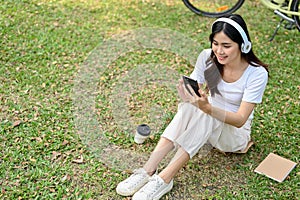 Beautiful Asian woman listening to music, using her phone, taking a rest in the public park