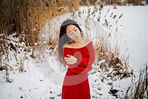 Beautiful asian woman in long red dress near the reeds over winter background. Fairy tale girl on winter landscape.