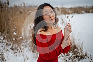 Beautiful asian woman in long red dress near the reeds over winter background. Fairy tale girl on winter landscape.