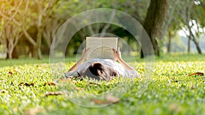 A beautiful Asian woman lying and reading a book on the grass.Concept of recreation, education and study , curiosity, leisure time